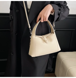 Detailed view of a cream leather crossbody bag with lychee grain texture and top handle