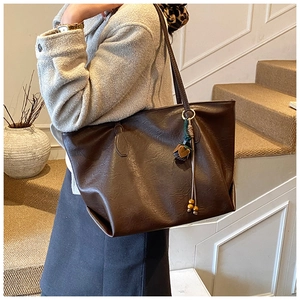 Detail view of deep brown litchi grain leather tote bag with wooden bead pendant accessory