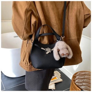 Detail of black leather hobo bag with silver clasp and plush rabbit pendant on model
