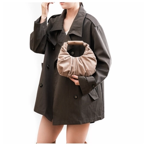 Detail of beige pleated suede handbag with smooth handle worn with a trench coat