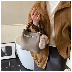 Detailed view of gray litchi texture bucket bag with a plush rabbit charm and silver clasp