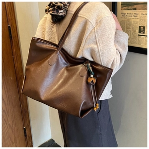 Macro detail of dark brown leather tote bag with vintage leaf charm and wooden bead