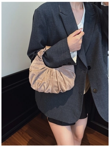 Detail of soft pleated cloud handbag in champagne gold fabric paired with grey blazer