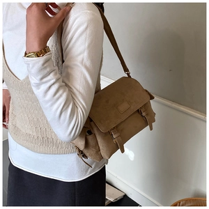 Brown suede messenger bag with buckle detail worn by a model in a casual outfit