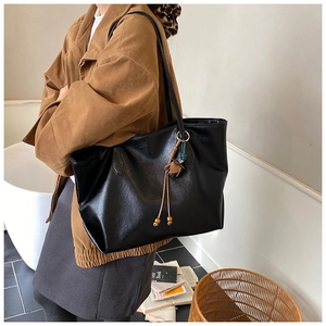 Fashionable black large tote bag with tassel charm worn over the shoulder for daily commute