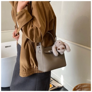 Detail of grey lychee leather handbag with metal turn-lock and plush bunny charm