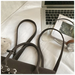 Detail of dark brown leather bag with silver eyelets and a grey fluffy keychain