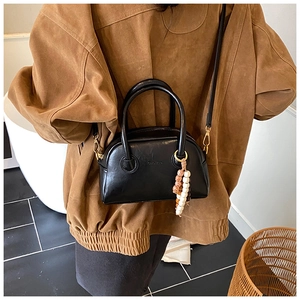 Détail d'un sac baguette noir semi-circulaire avec des pampilles en perles de bois colorées