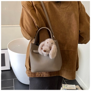Brown litchi leather bucket bag with cute plush bunny charm shown on model's shoulder
