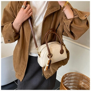 Detail of cream Boston bag with brown handles and a decorative beaded charm