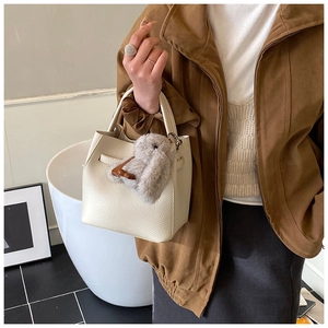 Close-up of creamy white lychee grain leather bucket bag with plush bunny charm