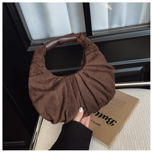 Detail of vintage brown pleated suede shoulder bag with smooth dark handle in a warm setting