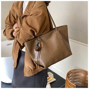 Detail of a large brown tote bag with retro tassel charm and slim shoulder straps