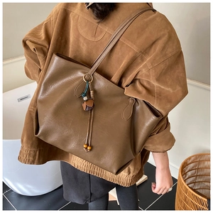 Brown leather tote bag with tassel pendant shown on shoulder for daily commuting