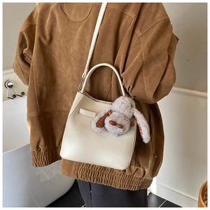 Detail of a beige bucket bag with a plush rabbit charm and a detachable strap