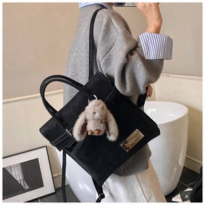Detail of black leather backpack with plush bunny keychain and metal brand plaque
