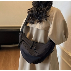 Detail of a black crescent crossbody bag with braided rope zipper on a trench coat