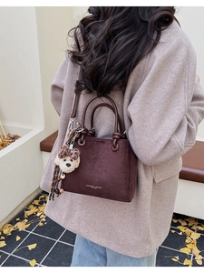 Outdoor street style view of dark brown suede bucket bag with cute bear charm