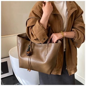 Close-up of a large tan leather tote bag with stylish tassel detail worn over the shoulder