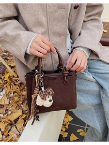 Detail of a dark brown suede bucket bag featuring a leopard dog plush and striped tassel charm
