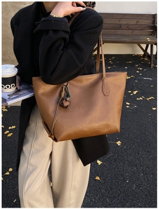 Brown leather tote bag featuring a flower pendant charm in an outdoor autumn setting