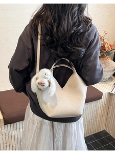 Sac seau chic blanc cassé à grain litchi porté à l'épaule par un mannequin en salle