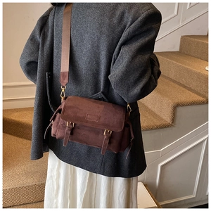 Detail of a brown suede crossbody bag with wide strap on a model in gray blazer