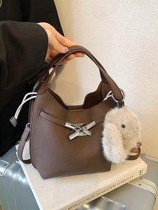 Brown leather bucket bag with silver buckle, plush rabbit charm, and crossbody strap