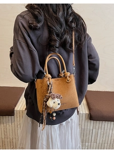 Brown suede bucket bag with plush puppy charm shown on model in a casual daily outfit