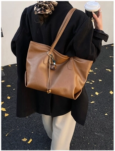 Detail view of brown PU leather tote bag with tassel charm worn on shoulder
