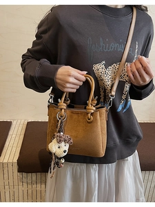 Detail of brown suede crossbody bag with dual handles and a white plush puppy charm