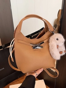 Caramel bucket handbag with silver cross buckle and plush rabbit charm in lifestyle setting