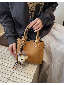 Detail of brown suede bucket bag with knot handle and plush puppy charm accessory