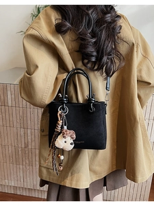 Detail of black suede handbag featuring a plush dog charm and leopard print tassel