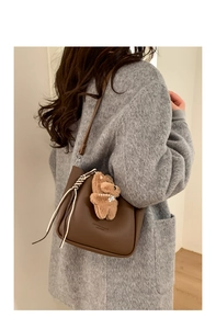 Close-up of a dark brown lychee leather bucket bag featuring a cute plush bear charm