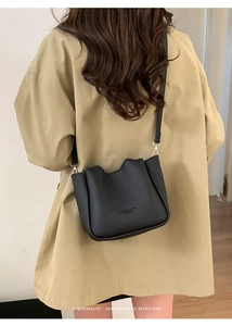 Black pebbled leather bucket bag with wavy top edge worn over a long khaki trench coat