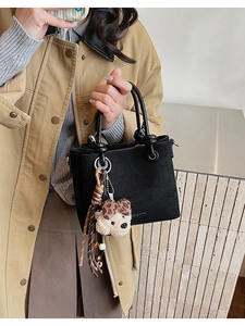 Detail of black suede bucket bag with round handles and plush puppy charm accessory