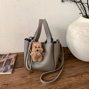 Detail of grey lychee leather bucket bag with cute plush dog charm on wooden table