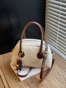 Vintage beige leather bowling bag with brown handles and bead charm on wooden surface