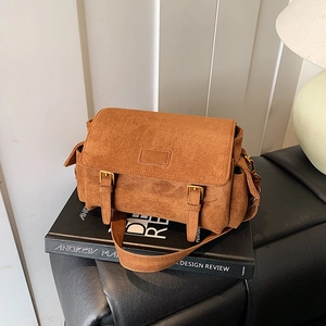 Brown faux suede messenger bag with dual buckles shown on a book in lifestyle setting