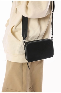 Side view of black leather crossbody bag with wide strap on casual beige outfit