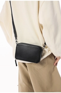 Detail of a black rectangular mini crossbody bag with double zippers and adjustable strap