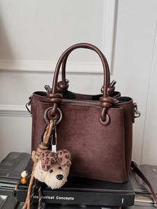 Dark brown matte bucket bag with dual handles and plush dog charm on vintage books