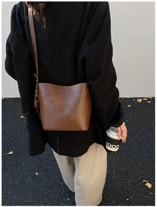 Brown leather bucket bag shown on shoulder in a stylish street style street setting