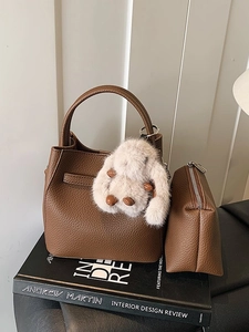 Brown litchi grain leather bucket bag with fluffy rabbit charm on design books