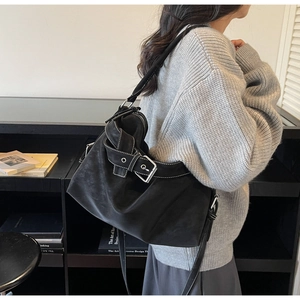Detail of black tote bag with white contrast stitching and decorative buckle on model