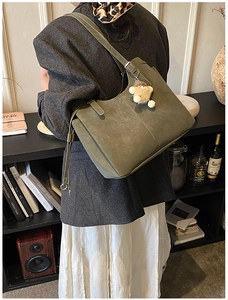 Detail of olive green suede tote bag with plush charm against a vintage bookshelf