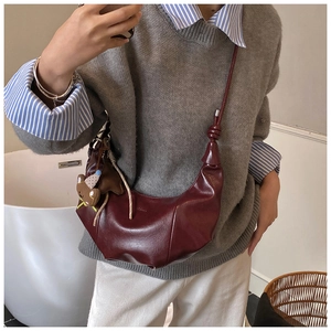 Detail der weinroten Leder-Tasche mit Bärenanhänger und geknotetem Schulterriemen-Design