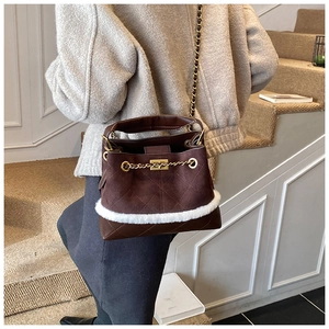 Close-up of quilted dark brown suede bucket bag with white faux fur trim and gold chain detail