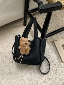 Elegant black lychee texture bucket bag with cute brown plush dog charm on white carpet